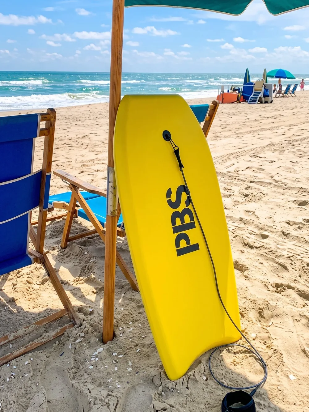 Gelbes Boogie Board unter einem Sonnenschirm neben Holzstühlen